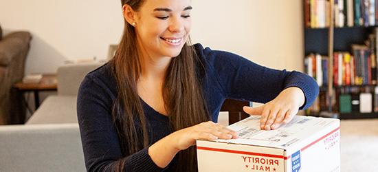 Young woman labeling a 美国邮政总局 优先邮件 国际 package.